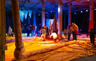 Niñas y niños juegan en una nave industrial con piezas de tela