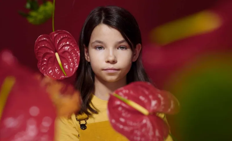 Niña tras unas flores rojas