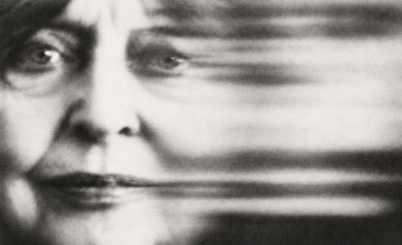 Fotografía en blanco y negro del rostro de una mujer adulta con un haz borroso al lado