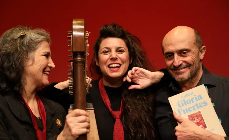 Dos mujeres y un hombre con una guitarra y un libro sonríen