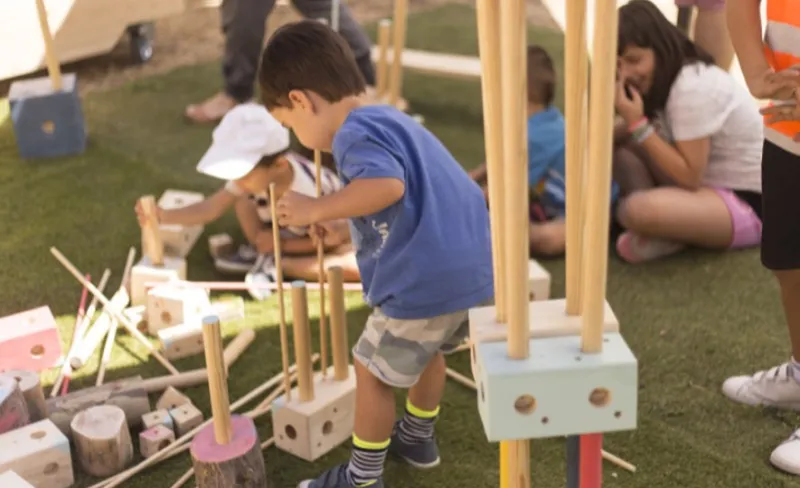 Niñas y niños jugando con las piezas de madera del juego el Gran Convoy en Matadero Madrid.
