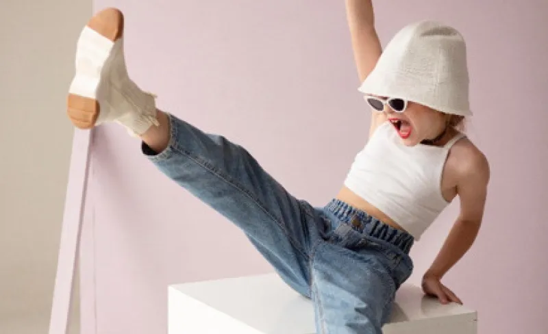 Niña con gafas de sol bailando sobre un cubo blanco