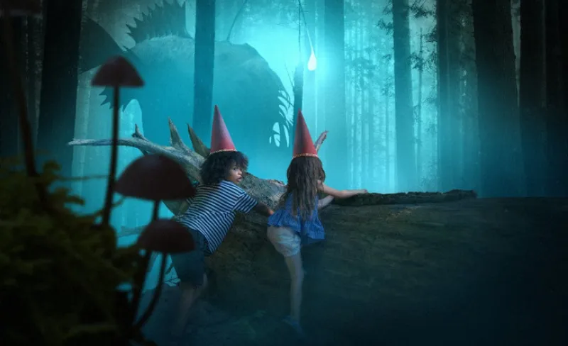Niños vestidos de hada, se asoman detrás de un tronco en un oscuro bosque
