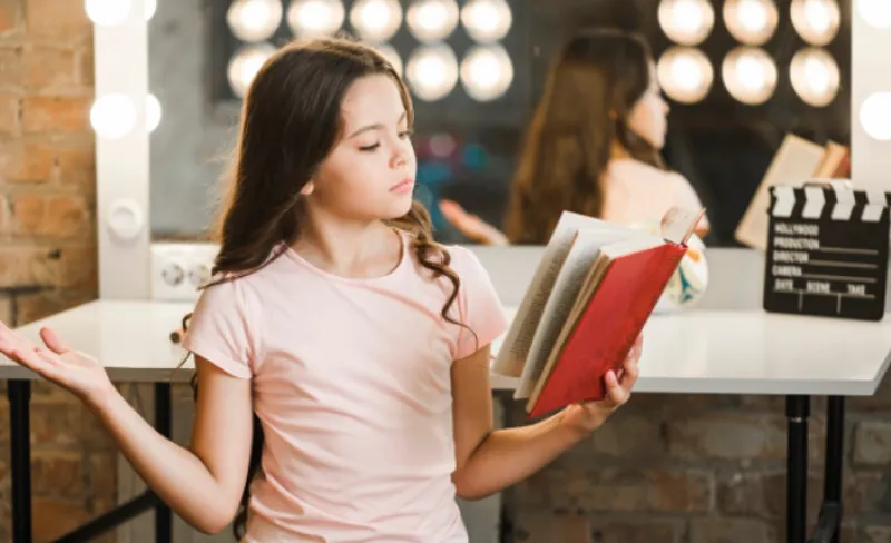 Niña ojea un libro con un espejo detrás