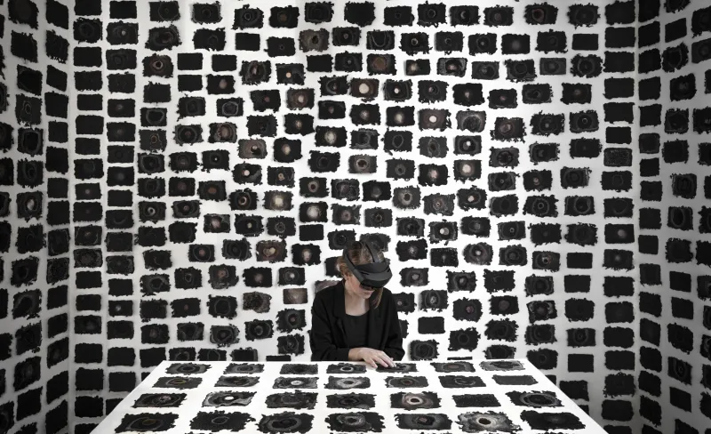 Una mujer con gafas de realidad virtual está sentada a una mesa con un montón de recuadros negros rodeándola