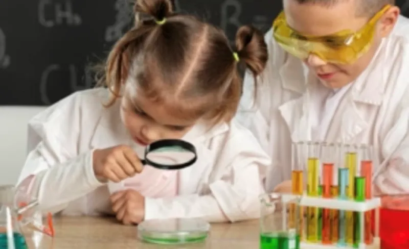Una niña observa algo con lupa y un niño la mira