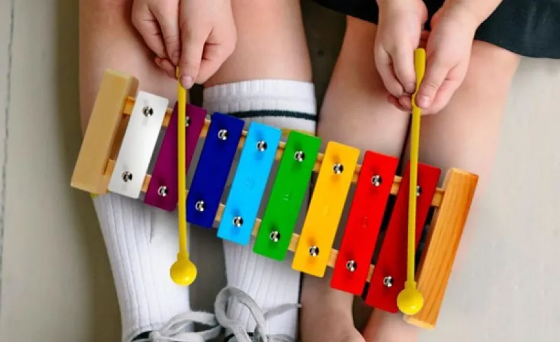 Las piernas de una niña y un niño sujetan un xilófono de colores
