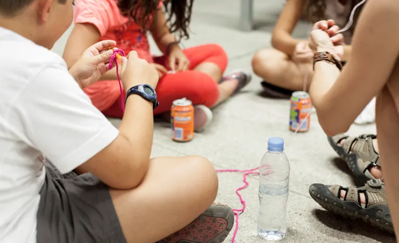 niñas y niños juegan con latas e hilos sentados en el suelo