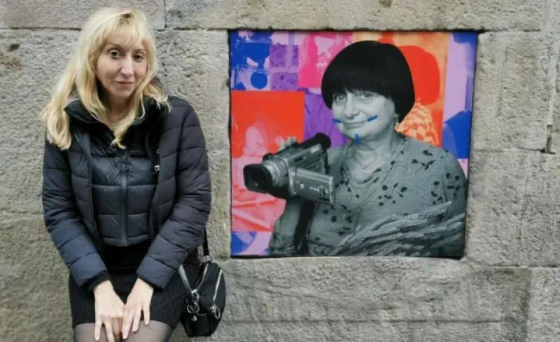 Una mujer posa junto a un cartel de otra mujer vandalizado