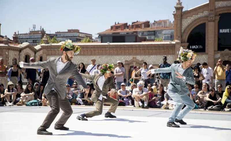 tres hombrs trajeados con flores en la cabeza bailan frente al público al aire libre