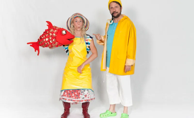 Chico y chica disfrazados de marineros con chubasquero amarillo y un muñeco de un pez rojo en la mano