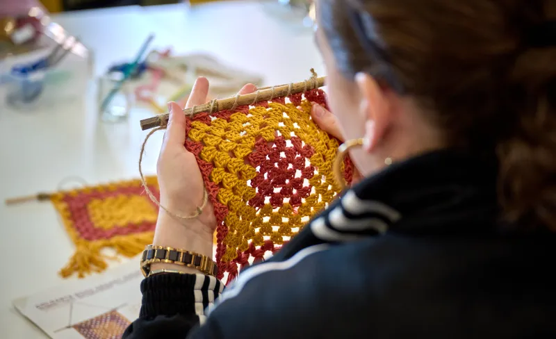 una mujer teje una pieza de tela en colores amarillo y rojo