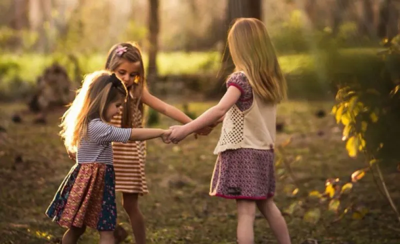 Tres niñas bailan en un bosque otoñal dándose la mano