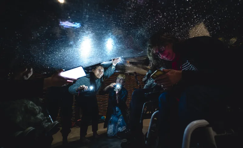 una chica ríe jugando iluminada por una linterna bajo una cortina