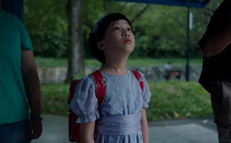 UNA NIÑA ORIENTAL MIRA HACIA EL CIELO. LEVA UNA MOCHILA COLGADA A LA ESPALDA