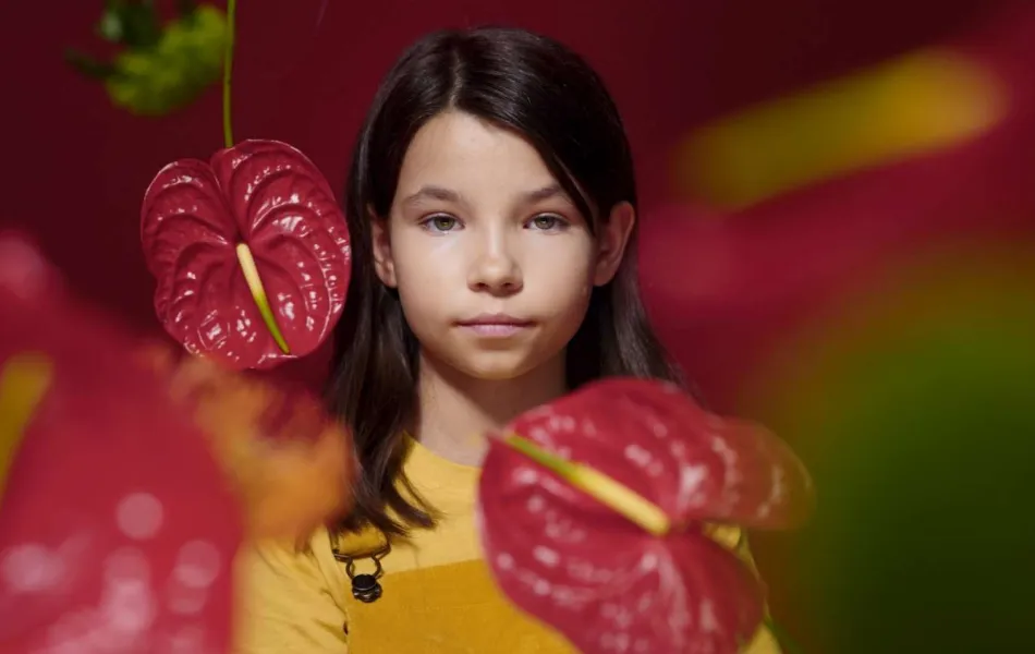 Niña tras unas flores rojas