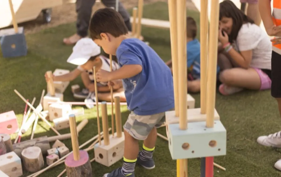 Niñas y niños jugando con las piezas de madera del juego el Gran Convoy en Matadero Madrid.