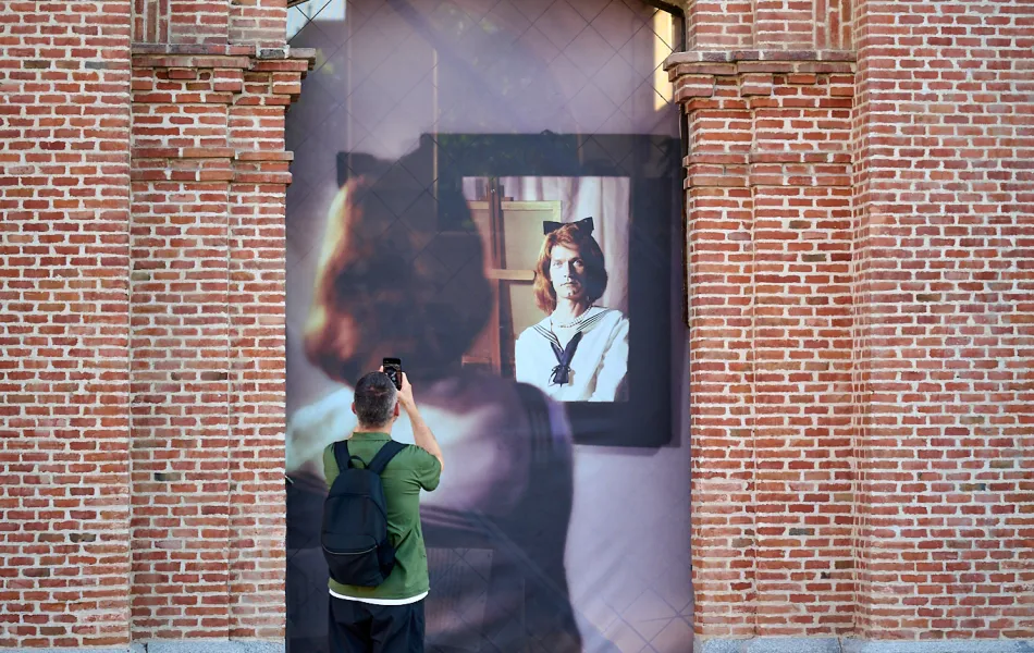 Un hombre fotografía una foto en formato grande que ocupa un vano en una pared de ladrillo