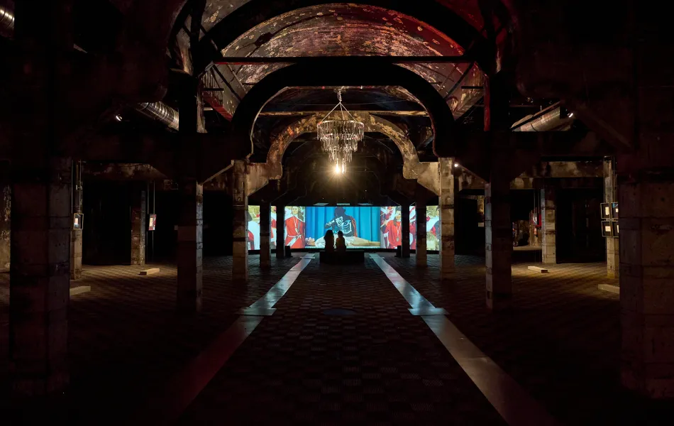 Nave industrial a oscuras con una gran lámpara iluminada y pantallas al fondo