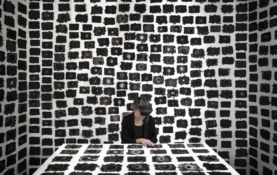 Una mujer con gafas de realidad virtual está sentada a una mesa con un montón de recuadros negros rodeándola