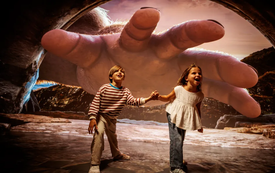 Niña y niño de la mano disfrutan con una imagen de una mano gigante tras ellos