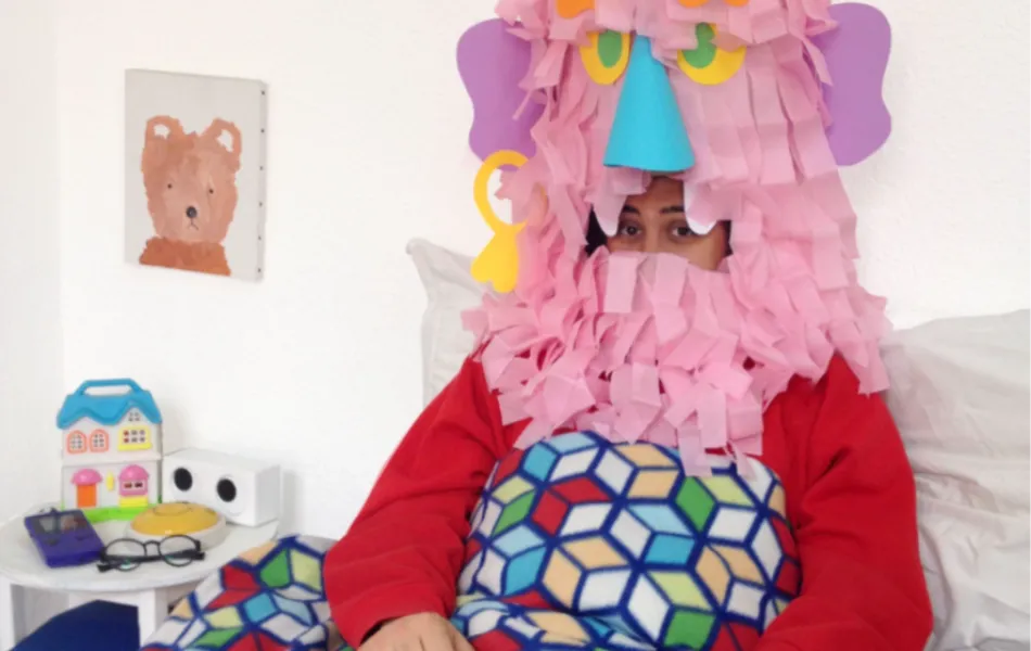 Una persona disfrazada de monstruo rosa está sentado en su cama