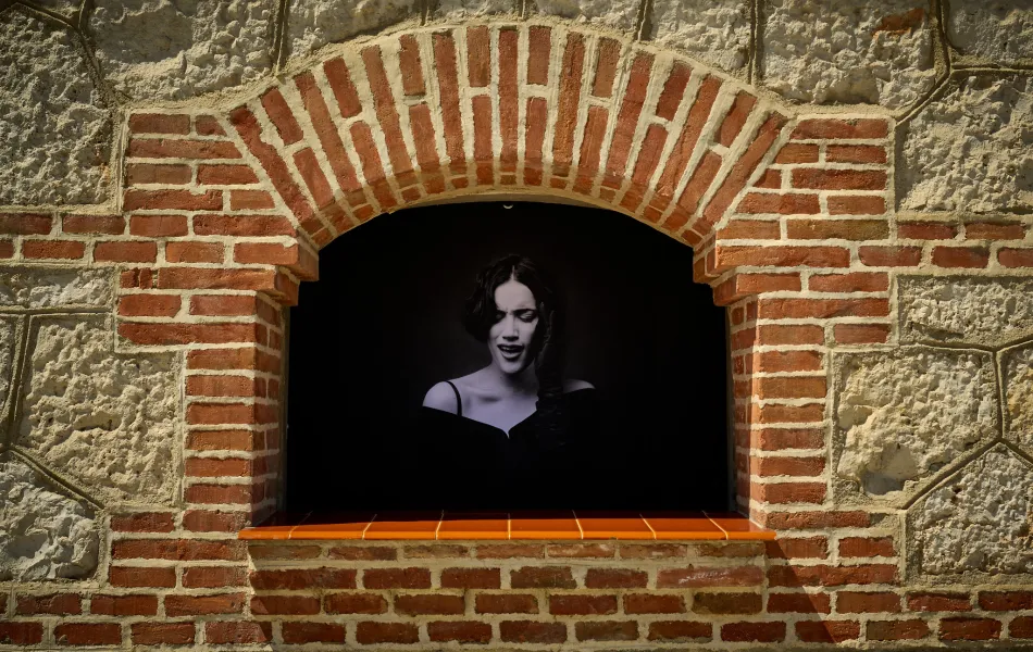 Foto de una chica cantando en blanco y negro dentro de una ventana de un edificio de ladrillo estilo neomudéjar