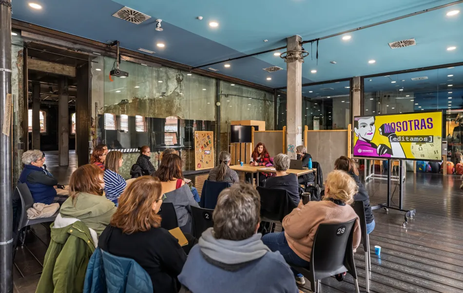 Mujeres escuchan a dos ponentes durante la celebración de una Editatona de Wikipedia en un espacio amplio acristalado