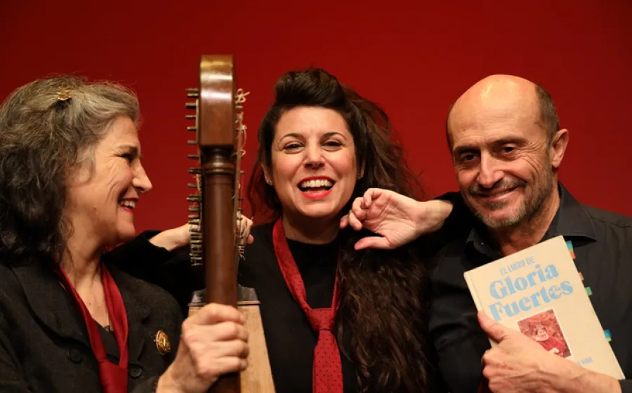 Dos mujeres y un hombre con una guitarra y un libro sonríen
