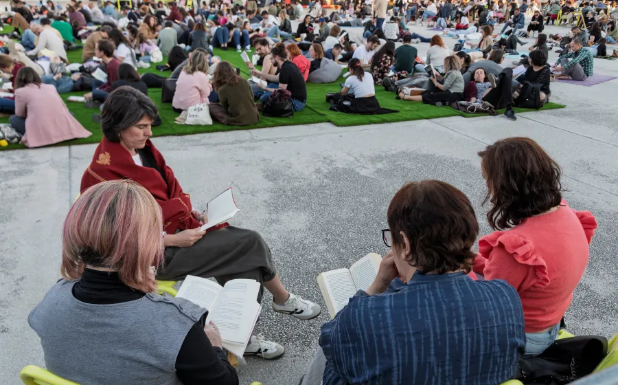 Personas leyendo sentadas en sillas con gente sentada en el suelo de fondo