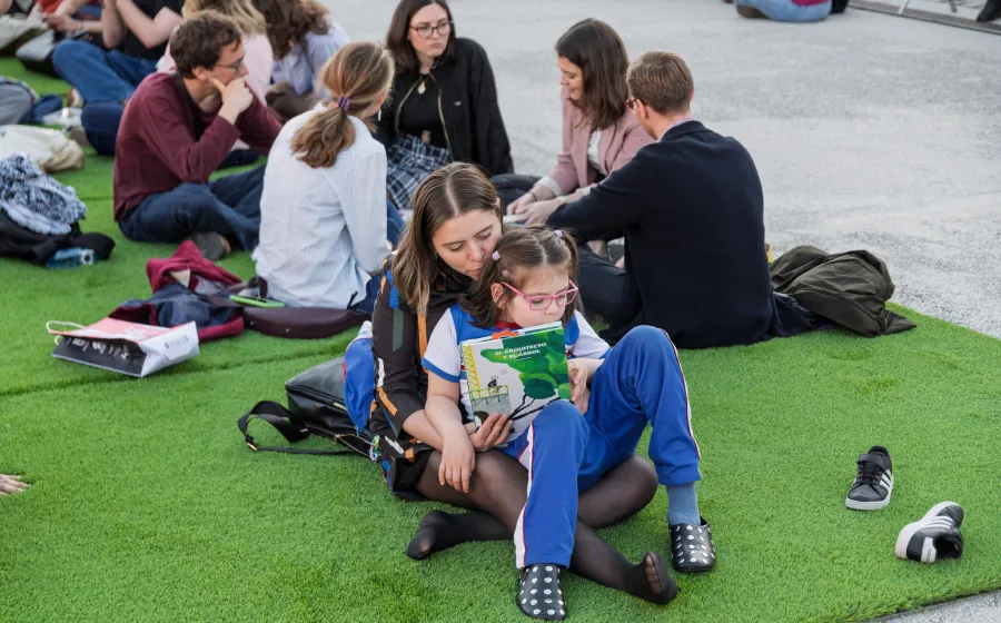 Madre e hija leen sentadas sobre cesped artificial