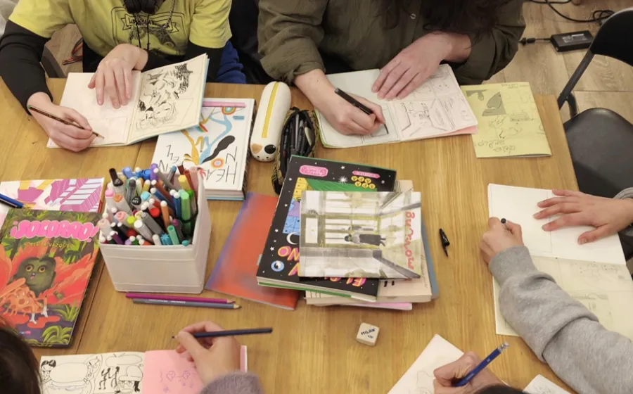 materiales de dibujo sobre una mesa y manos que lo manejan