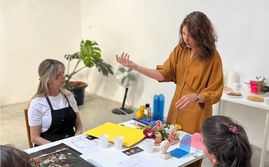 Mujer explica algo a otras dos mujeres con elementos sobre una mesa