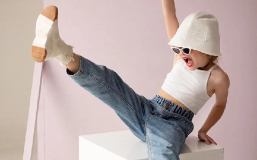 Niña con gafas de sol bailando sobre un cubo blanco