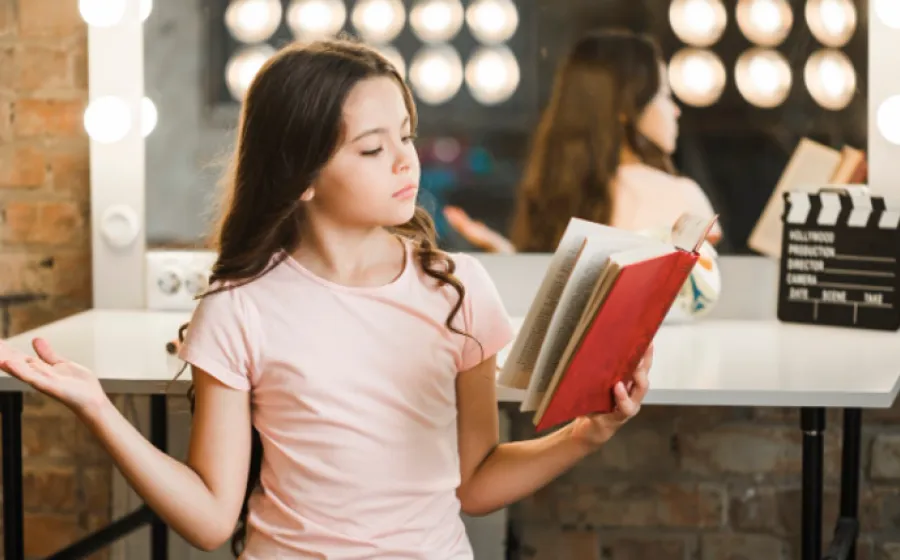 Niña ojea un libro con un espejo detrás