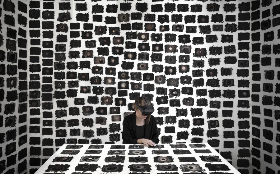 Una mujer con gafas de realidad virtual está sentada a una mesa con un montón de recuadros negros rodeándola