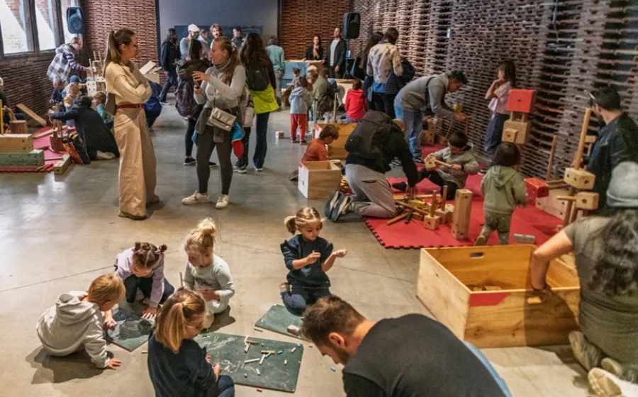 Madres padres y niños y niñas juegan con artilugios de madera en un espacio diáfano