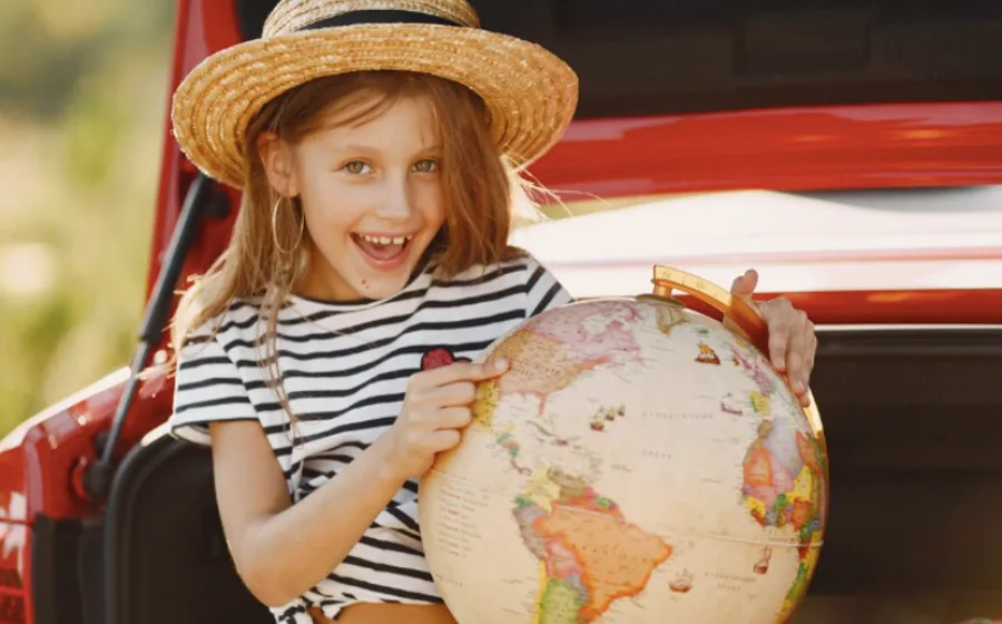 Niña con un sobrero de paja juega con una bola del mundo