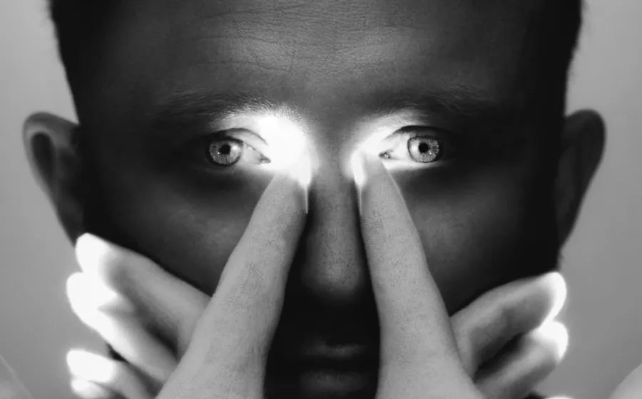 rostro de un hombre que apunta con sus dedos índices a los ojos iluminados
