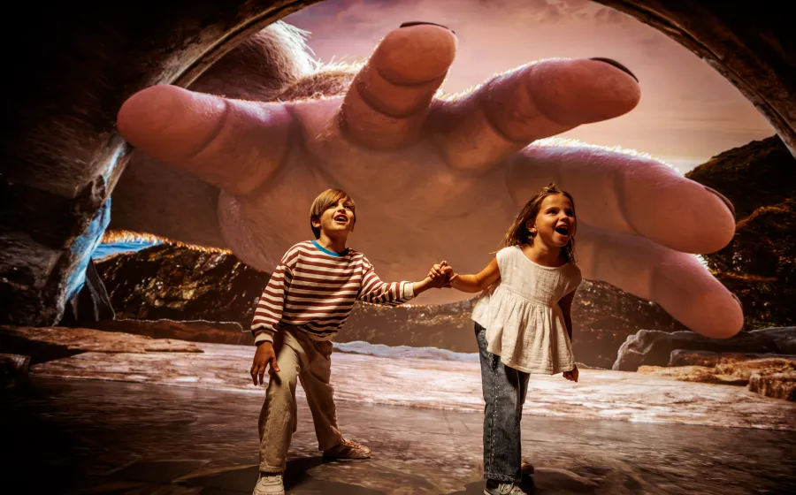 Niña y niño de la mano disfrutan con una imagen de una mano gigante tras ellos