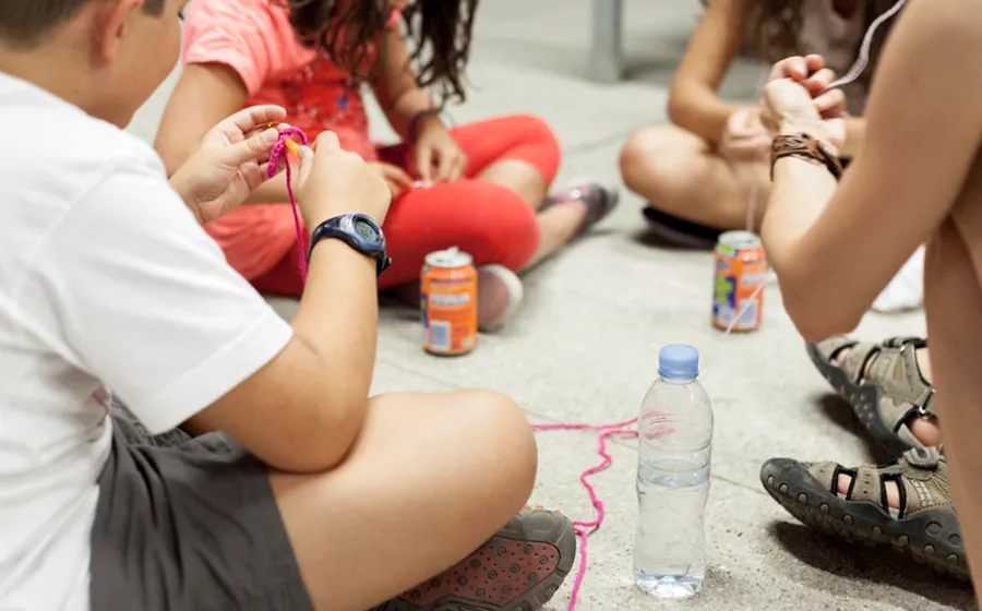 niñas y niños juegan con latas e hilos sentados en el suelo
