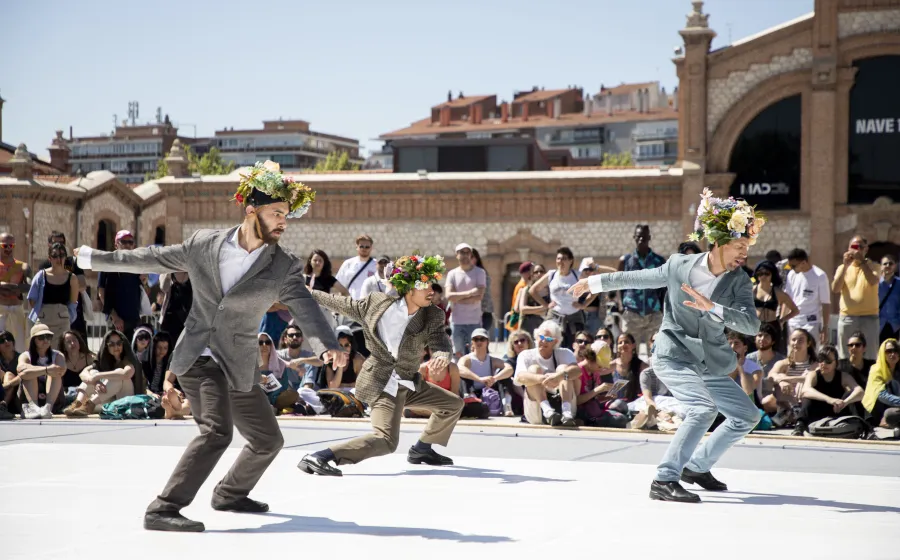 tres hombrs trajeados con flores en la cabeza bailan frente al público al aire libre