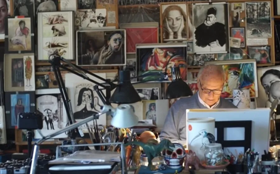Fotografía del director de cine Carlos Saura trabajando frente a un atril con una pared de fondo llena de cuadros