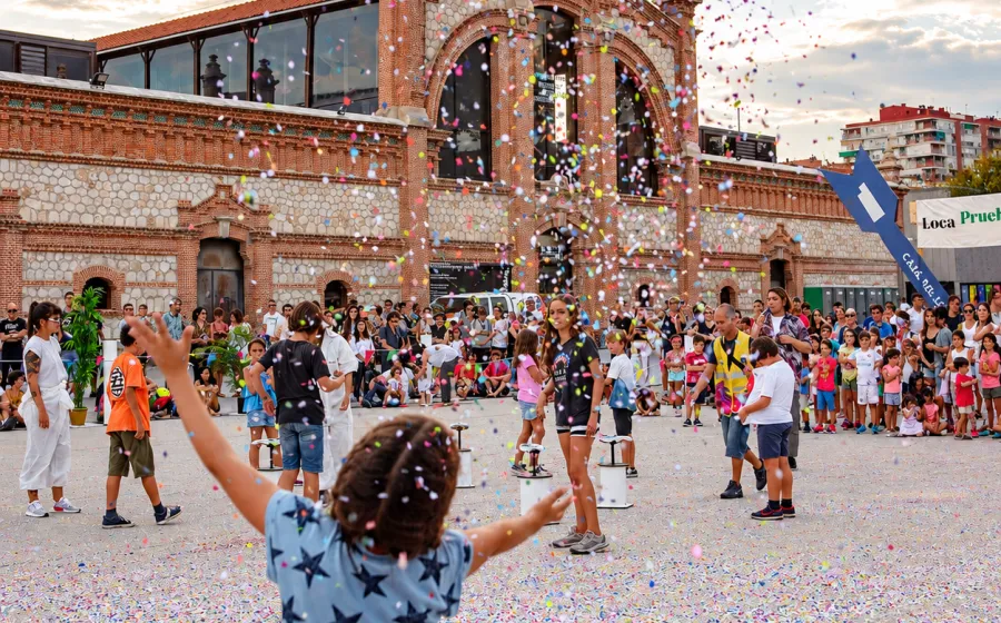 Una niña arroja confeti al cielo en una explanada junto a otros niños. De fondo un edificio del Matadero Madrid