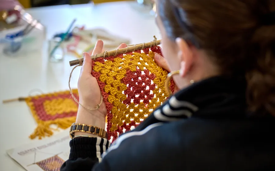 una mujer teje una pieza de tela en colores amarillo y rojo