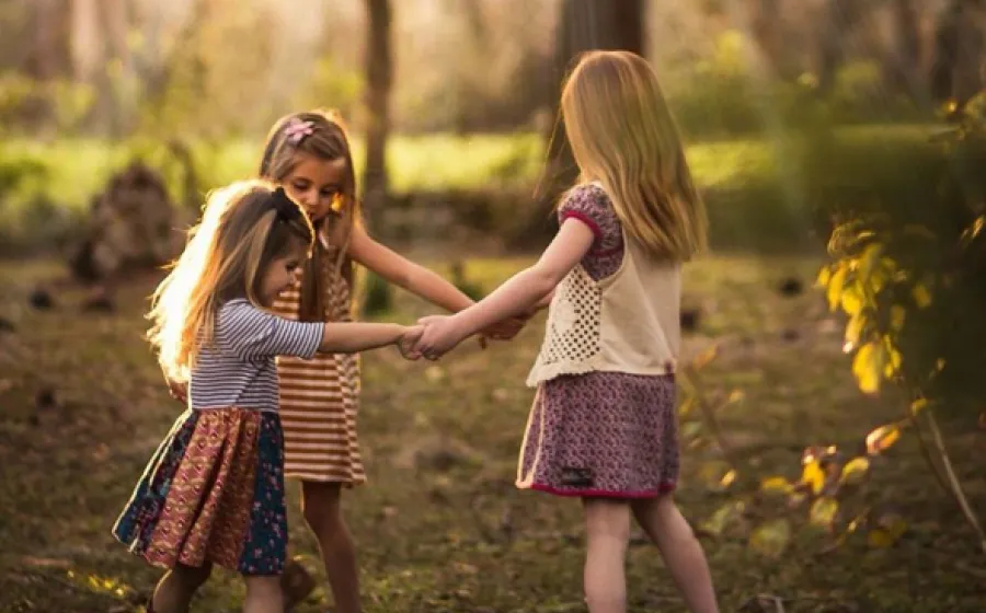 Tres niñas bailan en un bosque otoñal dándose la mano