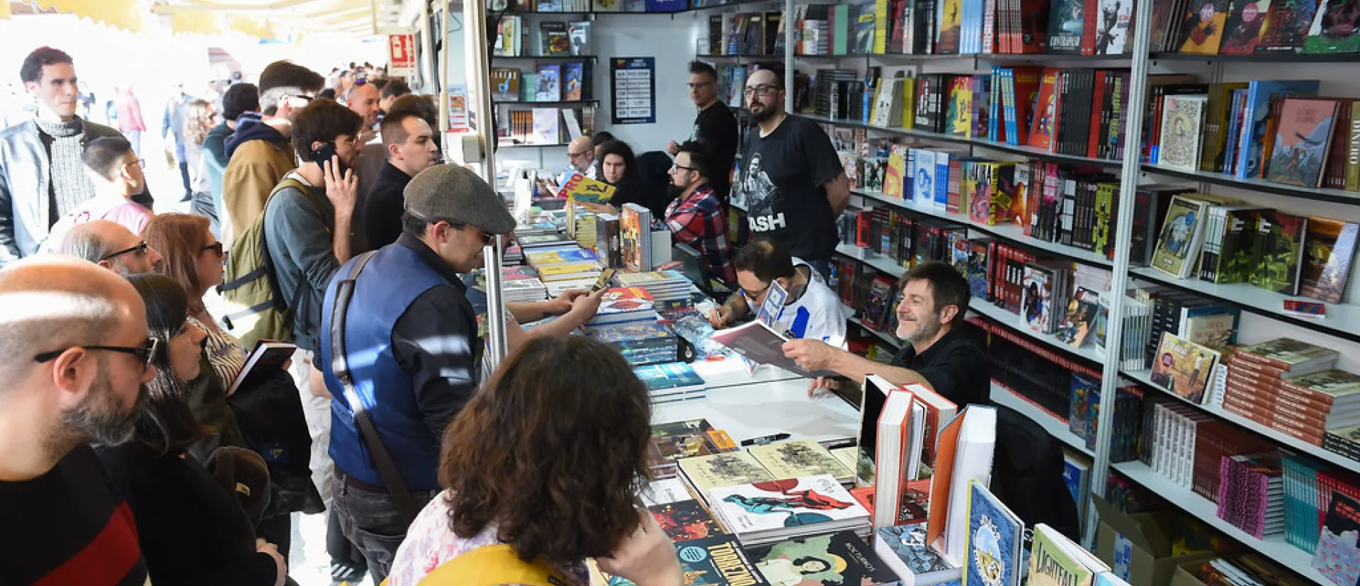 Gente mira los productos frente a un stand de librería en una feria