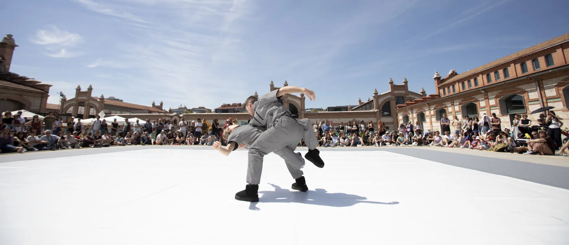 una pareja con un mono gris bailan en una superficie blanca al aire libre frente al público