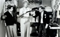 Hombre con bigote y sobrero, Groucho Marx, mira incrédulo a un forzudo que dobla una barra