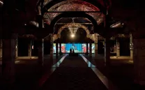 Nave industrial a oscuras con una gran lámpara iluminada y pantallas al fondo